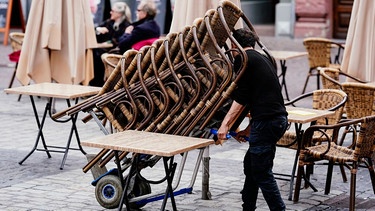 Der Mitarbeiter einer Gaststätte rollt einen Stapel Stühlee auf den Marktplatz | Bild: dpa-Bildfunk/Uwe Anspach