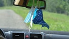 Mundschutzmasken hängen am Rückspiegel in einem Auto. | Bild: picture alliance / Winfried Rothermel