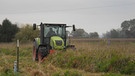 Traktor mit Mähwerk fährt bei trübem Wetter durch hüfthohen Grasbestand. Links im Bild ein Pfahl. | Bild: BR / Ursula Klement