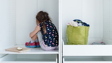Ein Mädchen kauert in einer Schrankecke mit dem Rücken zum Betrachter. | Bild: picture-alliance / Markus Scholz