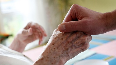 Ein Pfleger hält die Hand einer Bewohnerin eines Pflegeheims | Bild: picture-alliance/dpa