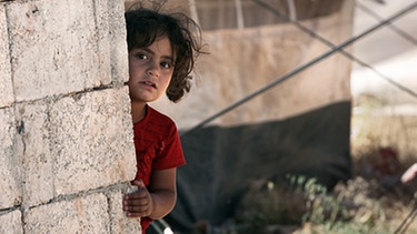Kleines Mädchen blickt hinter Mauer hervor | Bild: picture-alliance/dpa