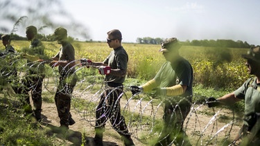 Soldaten ziehen einen Stacheldrahtzaun an der Grenze der Balkan-Flüchtlingsroute (Archiv) | Bild: picture-alliance/dpa