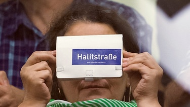 Ein Frau auf der Zuhörertribüne hält am 25.07.2017 im Gerichtssaal in München (Bayern) eine Handhülle hoch, auf der "Halitstraße - NSU Komplex auflösen !" steht. Vor dem Oberlandesgericht wurde der Prozess um die Morde und Terroranschläge des "Nationalsozialistischen Untergrunds" (NSU) fortgesetzt.  | Bild: dpa-Bildfunk/Peter Kneffel