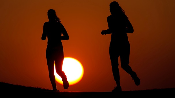 Zwei Frauen joggen in München in der Abendsonne durch einen Park | Bild: Sven Hoppe/dpa 