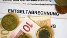 Auf Lohn- und Gehaltsabrechnungen (Entgeltabrechnungen) liegen Euromünzen und Eurogeldscheine. | Bild: picture-alliance/dpa