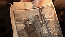 Ein Überlebender des NS-Massakers in Distomo (Griechenland) hält vor der Deutschen Botschaft in Athen am 6. Januar 2011 eine Kerze und ein Zeitungsbild von 1948, auf dem er und seine Schwester vor dem Grab der Eltern und des Bruders stehen | Bild: picture-alliance/dpa