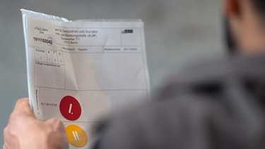 Ein Flüchtling aus Ãgypten hält am 19.11.2015 in der Registrierungsstelle für Flüchtlinge in Berlin seinen Fragebogen, auf dem die ersten beiden Stationen seiner Registrierung mit einem gelben und einem roten Aufkleber markiert sind. | Bild: picture-alliance/dpa/ Soeren Stache