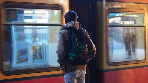 Ein junger Migrant mit einem Rucksack steht auf einem S-Bahn-Gleis und ein Zug fährt gerade durch. | Bild: picture-alliance/dpa/Wolfram Steinberg