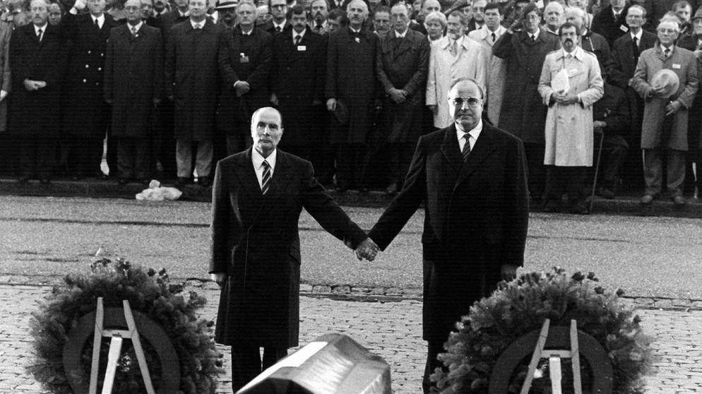 Der französische Präsident Francois Mitterrand (l) und Bundeskanzler Helmut Kohl (r) reichen sich über den Gräbern von Verdun die Hand - ein Symbol für die Aussöhnung zwischen Frankreich und Deutschland am 22.09.1984.  | Bild: picture-alliance/dpa