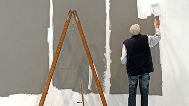 Ein älterer Herr streicht eine Wand | Bild: picture-alliance/dpa