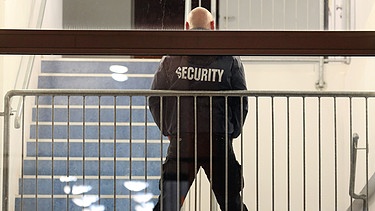 Ein Mitarbeiter einer Security-Firma steht in einem Treppenhaus.  | Bild: picture-alliance/dpa/Jan Woitas