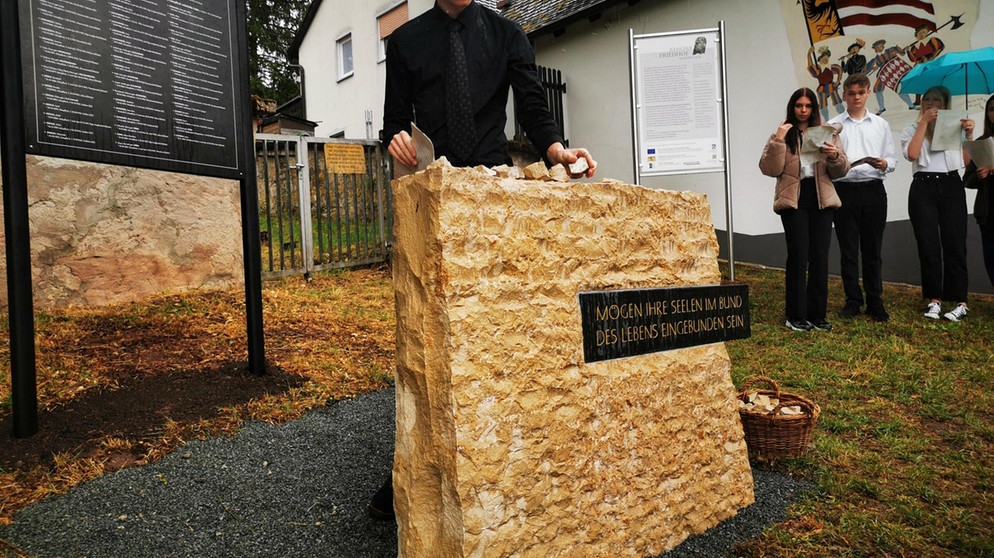 Ein schwarz gekleideter Schüler legt einen Stein auf einen Gedenkstein für die Opfer der Shoa in Schopfloch. | Bild: BR/Sophia Ruhstorfer