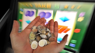 Ein Spieler hält vor einem Glücksspielautomaten Geld in seinen Händen | Bild: picture-alliance/dpa/Frank Leonhardt