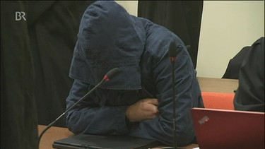 Angeklager und Kronzeuge sitzt im Gericht  und hat die Kapuze einer dunkelblauen Jacke  tief ins Gesicht gezogen um nicht erkannt  zu werden | Bild: Bayerischer Rundfunk