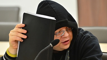 Der Thüringer Neonazi Tino Brandt im Landgericht in Gera (Thüringen) versucht mit einer Aktenmappe sein Gesicht zu bedecken | Bild: picture-alliance/dpa