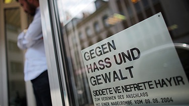 Ein Schild, das an den Nagelbomben-Anschlag vom 09.06.2004 erinnert, hängt am 2.6.2014 in der Keupstraße in Köln (Nordrhein-Westfalen) | Bild: picture-alliance/dpa
