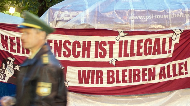 Ein Polizist geht an einem Plakat vorbei, mit dem Flüchtlinge in München für die Anerkennung ihrer Asylanträge protestieren | Bild: picture-alliance/dpa