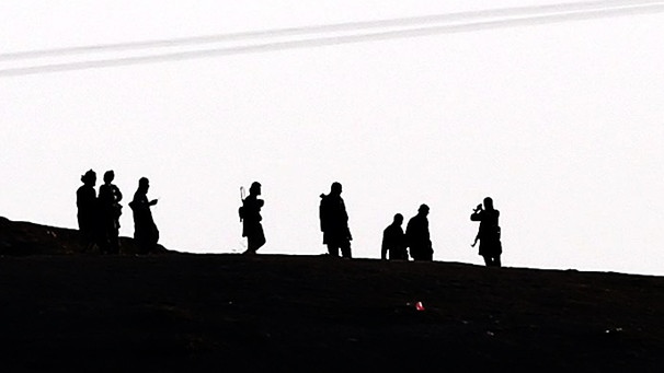 Kämpfer des Isalmischen Staates auf einer Anhöhe gehend im Gegenlicht fotografiert (Symbolbild). | Bild: picture-alliance/dpa