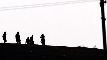 Kämpfer des Isalmischen Staates auf einer Anhöhe gehend im Gegenlicht fotografiert (Symbolbild). | Bild: picture-alliance/dpa