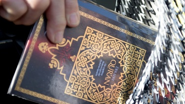 Symbolbild: Ein Mann verteilt kostenlose Koran-Exemplare an Passanten. | Bild: picture-alliance/dpa/Julian Stratenschulte