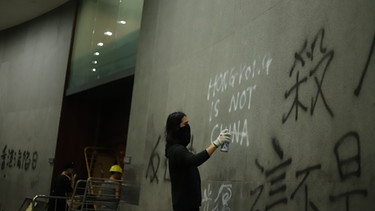 01.07.2019, China, Hongkong: Ein Demonstrant schreibt "Hongkong is not China"(Hongkong ist nicht China) an die Wand in einem Regierungsgebäude. Am Jahrestag der Rückgabe Hongkongs an China sind die seit Wochen andauernden Proteste in der Finanzmetropole eskaliert. Hunderte Protestler besetzten am Montagabend das Parlament der Stadt.  | Bild: dpa-Bildfunk/Liau Chung-Ren