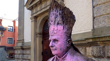 Die mit rosa Farbe besprühte Büste von Papst Benedikt XVI. vor der Kirche St. Oswald | Bild: Polizei Traunstein