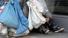 Hinter einem Einkaufswagen, der mit Plastiktüten behängt ist, sitzt ein Obdachloser. (Symbolbild)  | Bild: picture-alliance/dpa