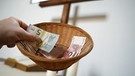 Eine Hand hält einen Sammelkorb mit Geld für die gottesdienstliche Kollekte | Bild: picture-alliance/dpa