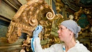 Eine Restauratorin repariert ein Muschelornament an der Seite einer Loge im Markgräflichen Opernhaus Bayreuth. | Bild: picture-alliance/dpa