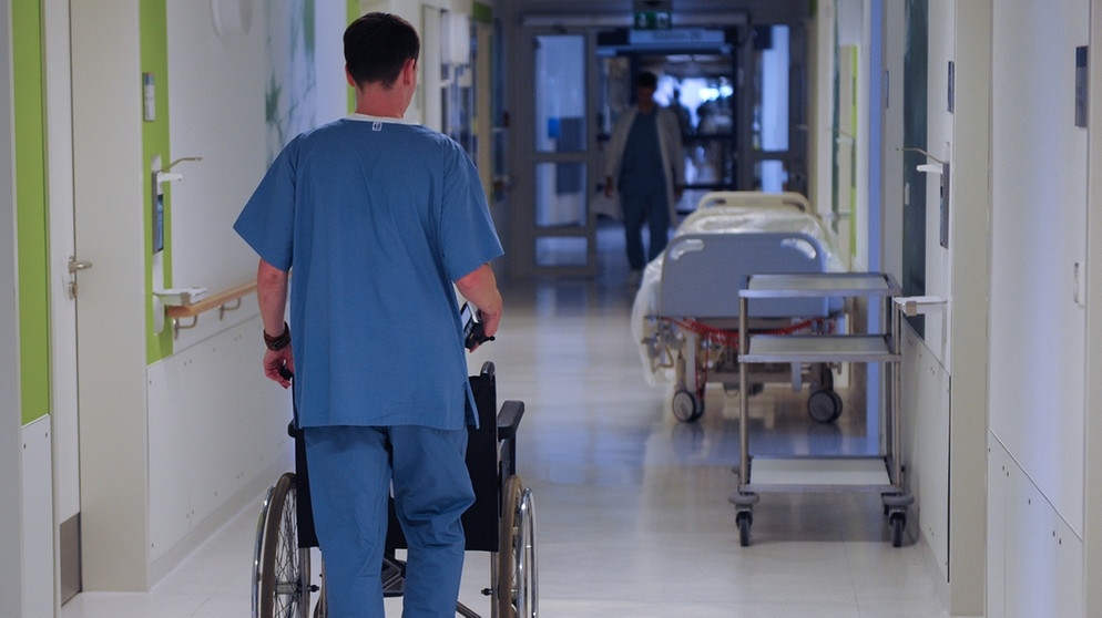 Ein  Pfleger schiebt im Krankenhaus einen patienten im Rollstuhl | Bild: pa/dpa/Peter Steffen