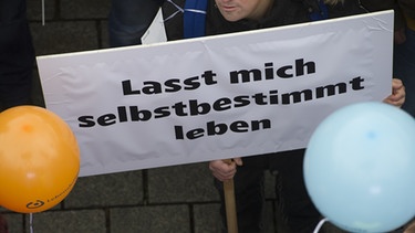 Ein Demonstrant hält während einer Kundgebung vor dem Brandenburger Tor ein Plakat. Zu der Demonstration am 7.11.2016 hatte die Bundesvereinigung "Lebenshilfe" aufgerufen, um ein besseres Bundesteilhabegesetz für Menschen mit Behinderung zu fordern. | Bild: dpa/picture-alliance/Paul Zinken