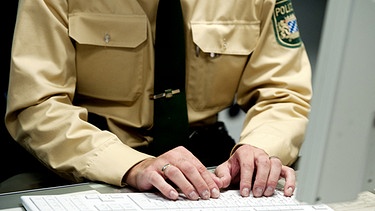 Symbolbild: Polizist schreibt auf einer Computertastatur | Bild: picture-alliance/dpa/Armin Weigel