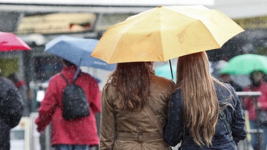 Zwei junge Damen unterm Regenschirm in einer belebten Fußgängerzone | Bild: picture-alliance/dpa