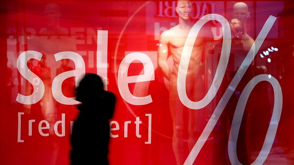 Eine Frau geht in Köln an einer Schaufensterabdeckung vorbei, die auf reduzierte Ware hinweist.  | Bild: picture-alliance/dpa