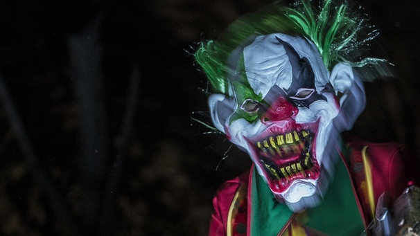 Weiß geschminkter Horror-Clown mit grünen Haaren, Mund weit aufgerissen, dunkler Hintergrund  | Bild: picture-alliance/dpa