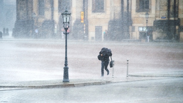 Ein Passant kämpft bei starkem Regen mit einem Schirm in den Händen gegen den Regen und den Wind auf dem Theaterplatz in Dresden (Sachsen) an. | Bild: picture-alliance/dpa