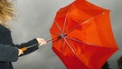 Junge Frau hält bei starkem Wind ihren orangen Regenschirm fest. | Bild: picture-alliance/dpa