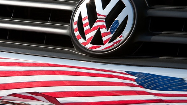 Die US-Fahne spiegelt sich  in Chattanooga (US-Bundesstaat Tennessee) in Logo und Kühlergrill eines Volkswagen-Fahrzeugs | Bild: picture-alliance/dpa/Friso Gentsch