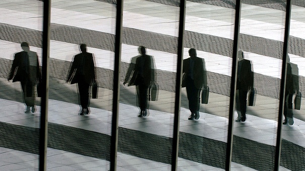 Ein Mann mit Aktentasche spiegelt sich  in den Glasscheiben eines Bürogebäudes | Bild: picture-alliance/dpa