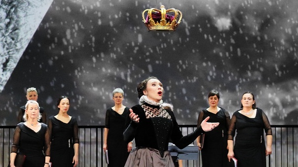 Anna Bolena (die historische Anne Boleyn) steht in Winterlandschaft, über ihr schwebt eine Krone. | Bild: © Marie-Laure Briane