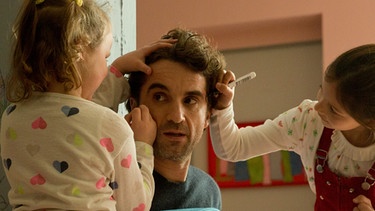 Filmszene aus "Das Leben ist kein Kindergarten - Umzugschaos". Hauptdarstelle Oliver Wnuk wird von seinen beiden Film-Kindern mit Stiften im Gesicht angemalt. | Bild: ARD Degeto, Volker Roloff