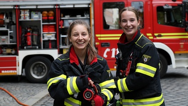Mit Feuerwehrfrau Lisi checkt Marina (links) wie die Arbeit bei der Feuerwehr ist und darf sogar auf einen richtigen Einsatz mitfahren! | Bild: BR/megaherz gmbh/Robin Worms