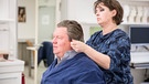 Maskenbildnerin Heike Puzicha bereitet Helmut Schleichs Haare für die Perücke vor und beklebt sie mit einer künstlichen Glatze – einer Art Gummihaube aus dem feinen Material Glazan – um die Übergänge besser zu kaschieren.  | Bild: BR / Philipp Kimmelzwinger
