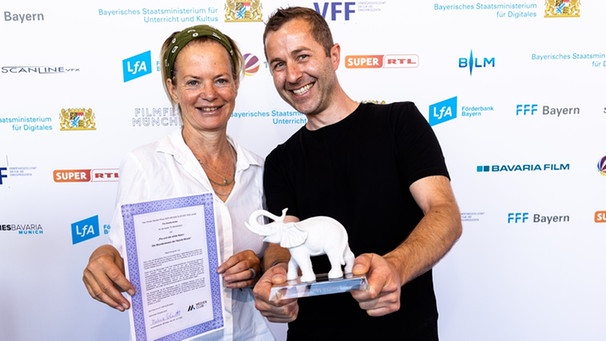 Dr. Stefanie Baumann (BR Redaktion Kinder) und Robert Sigl (Produktionsfirma Text & Bild) nehmen den weißen Elefanten stellvertretend für Pia Amofa-Antwi entgegen. | Bild: MCM / J. Müller