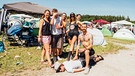 Eine glückliche Gruppe von Festival-Großwildjägern posiert mit ihrer Beute: ein Typ mit Sonnenbrille und weißem Shirt, der bäuchlings im Kiesweg am Campingplatz liegt. | Bild: BR/Johanna Schlüter