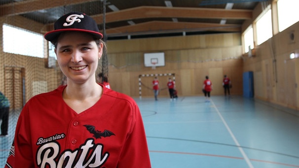 Gabi steht in einer Sporthalle und lächelt. Im Hintergrund ist ihr Team zu sehen.  | Bild: Cornelia Neumeyer