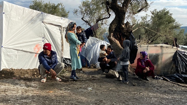 Bewohner des Flüchtlingslagers Moria auf der griechischen Insel Lesbos stehen und knien vor einem Zelt, im Hintergrund stehen Olivenbäume  | Bild: privat