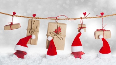 Eine Schnur mit kleinen Geschenken dran symbolisieren einen Adventskalender, dazwischen sind Wichtelmützen | Bild: mauritius-images
