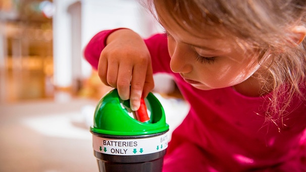 Ein kleines Mädchen schmeißt eine Batterie in einen Recyclingbehälter | Bild: mauritius-images